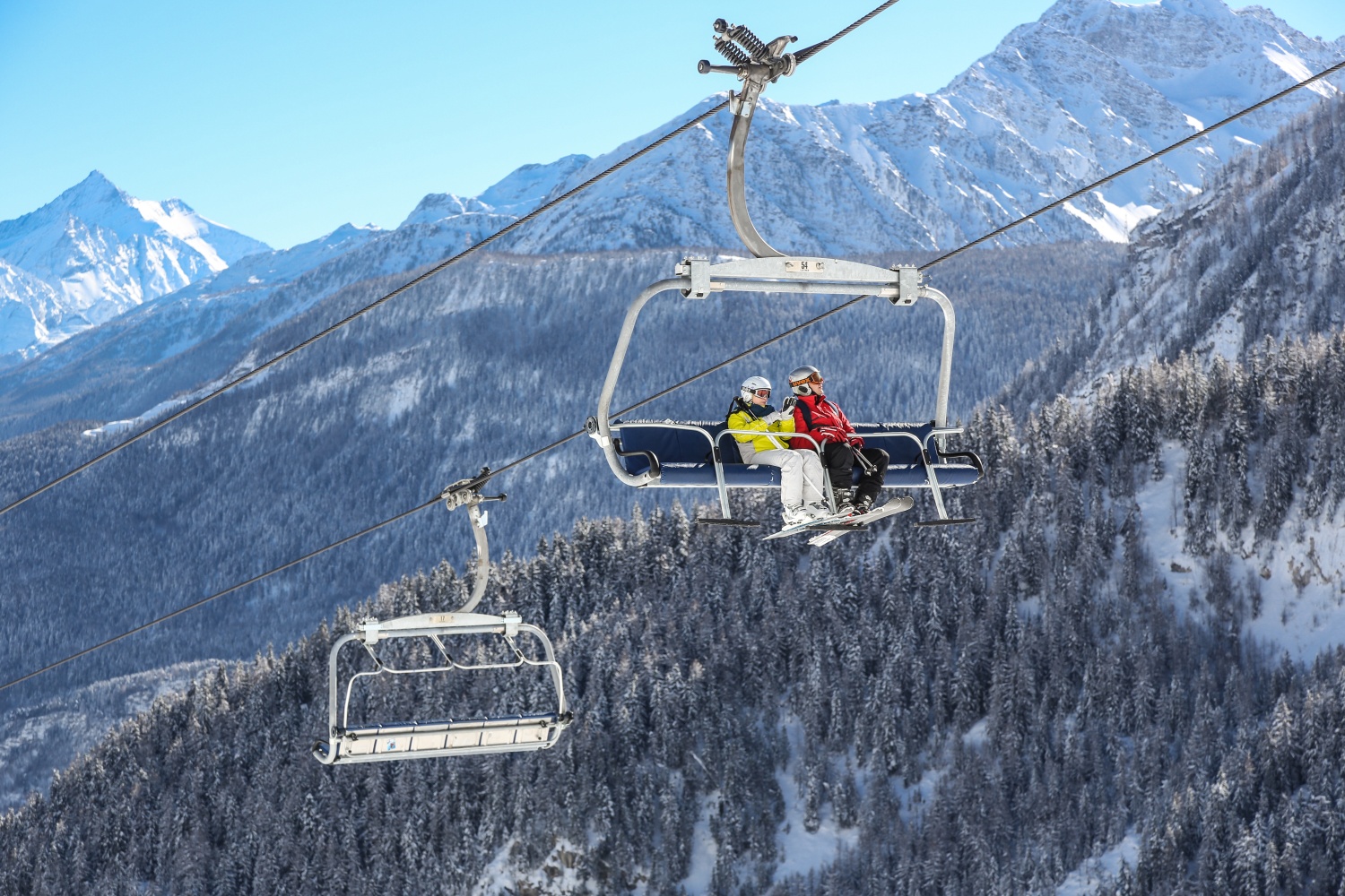 Couple sat on ski lift with mountains in background: Courmayeur, Valle d'Aosta