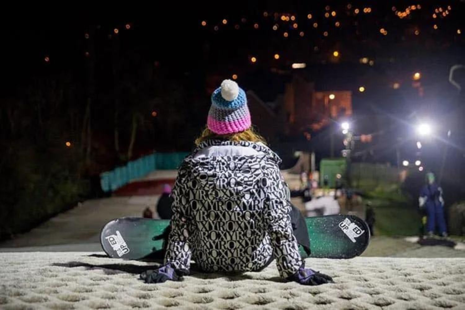 Woman snowboarder sat at top of dry ski slopes at night, Cardiff Ski and Snowboard Centre