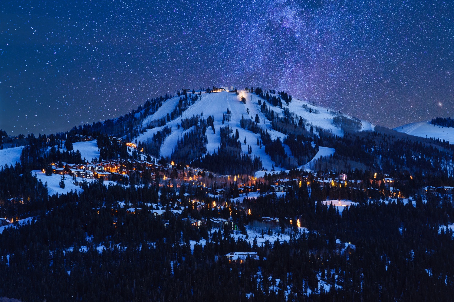 Deer Valley’s Bald Mountain and lit homes at night under a sky full of stars in Park City, UT
