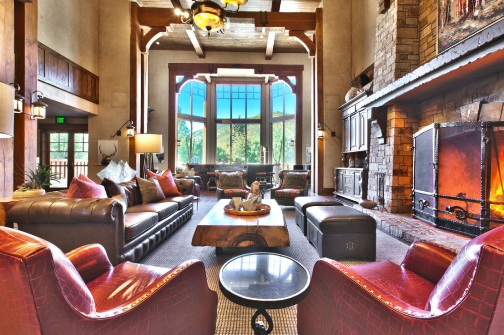 Chairs, a couch, and table in front of a roaring fireplace look out over scenic mountains from the lounge in Hotel Park City