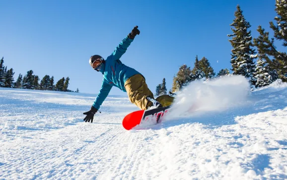 MainImage Man snowboarding and creating snowy dust cloud Skiing on a budget