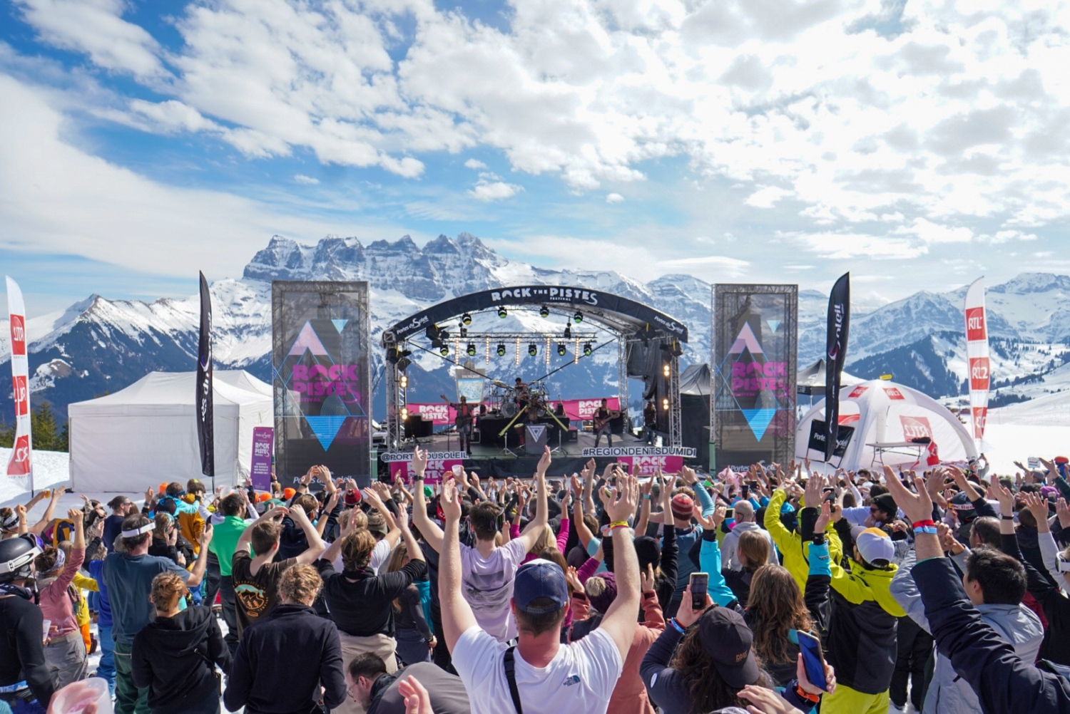 Crowds dancing to performers on stage with snowy mountains in background_Rock The Pistes Festival Review