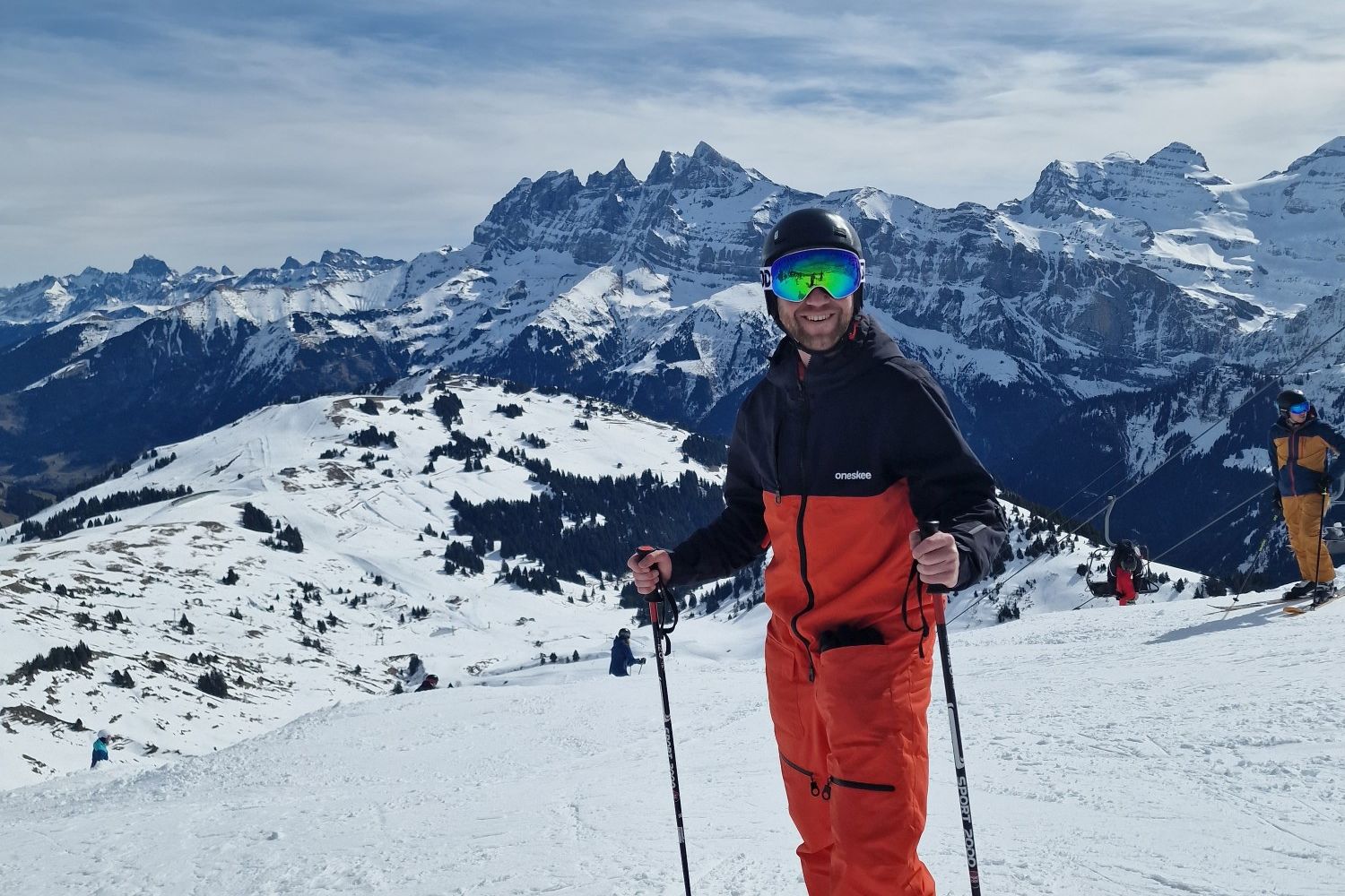 Skiing man stood on slope with snowy mountains in background_Rock The Pistes Festival 